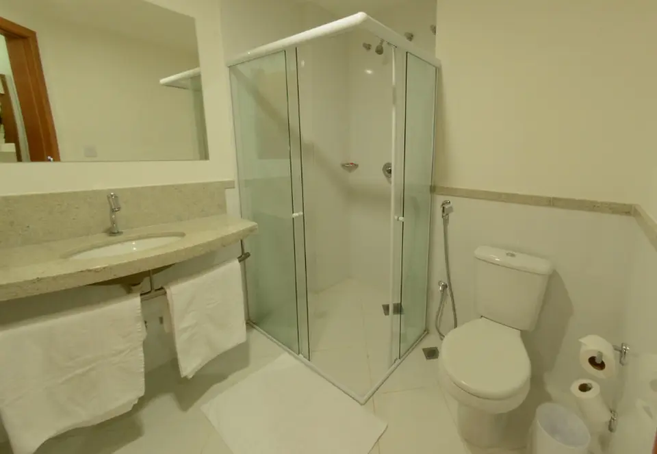 Banheiro do apartamento com box de vidro, bancada e toalhas