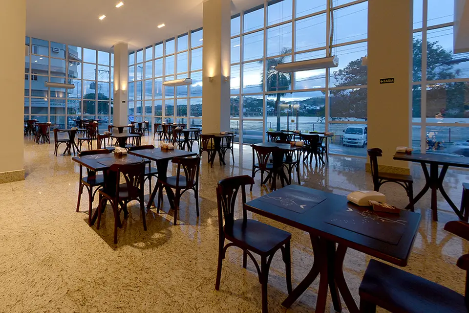 Salão do café da manhã com mesas e janelas para a cidade