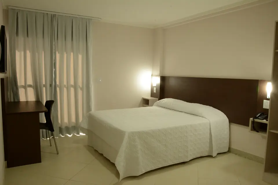 Apartamento casal com cama de casal, mesa de escritório e cortinas