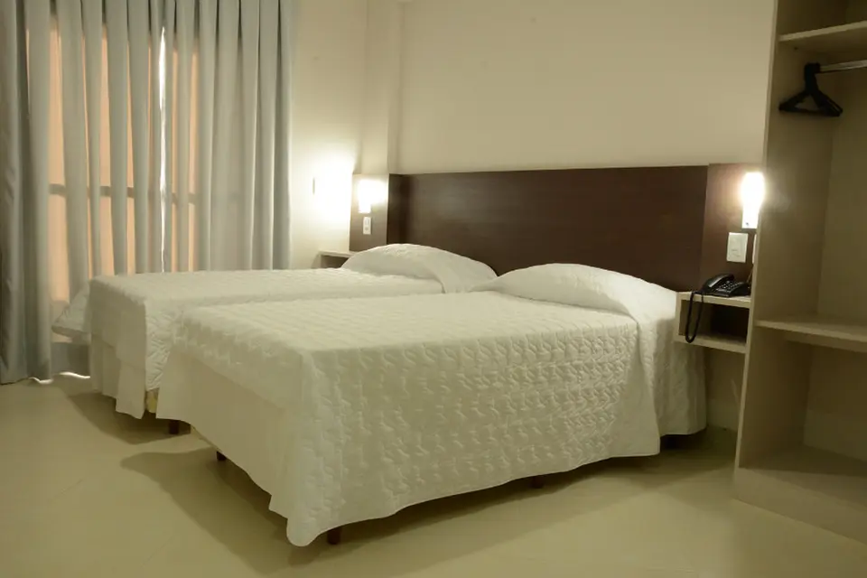 Apartamento duplo com duas camas de solteiro, cabeceira de madeira e mesa de escritório