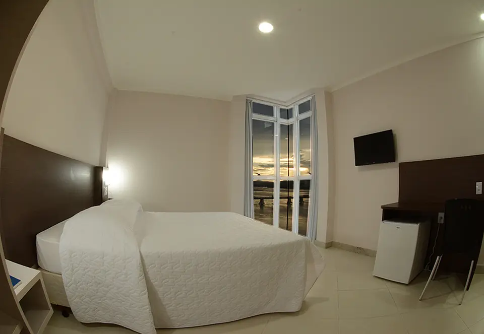 Apartamento single com cama, televisão e janela com vista da cidade ao entardecer